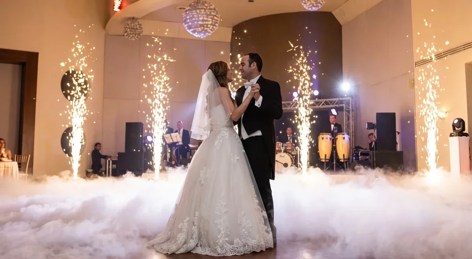 Novios en su primer baile con capa de humo bajo y fuentes de chispa fría, banda en vivo de fondo