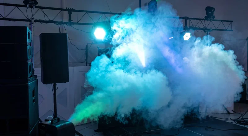 Escenario de concierto con niebla densa iluminada en azul y verde por las luces de escenario