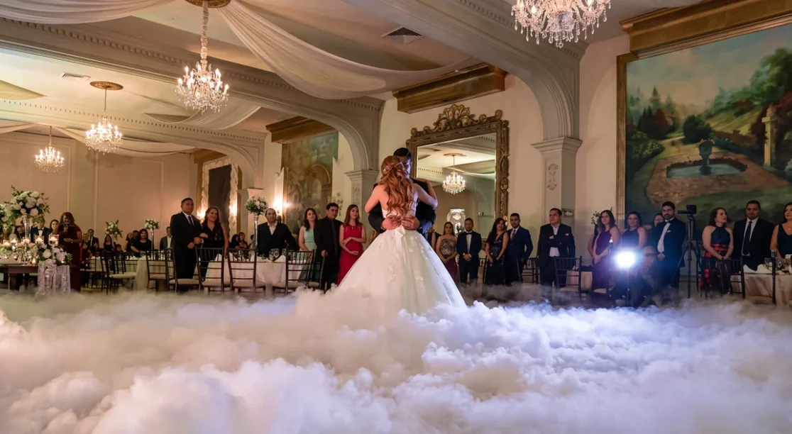 Novios en su primer baile flotando sobre una densa capa de humo bajo en un salón con candelabros