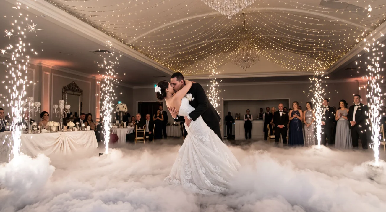 Novios en un beso dramático rodeados de fuentes de chispa fría, con los pies cubiertos por la capa de humo bajo