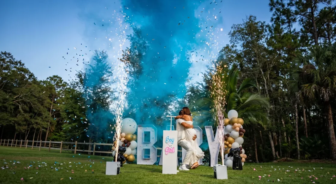 Pareja abrazada bajo una nube de humo azul con fuentes de chispa fría y confeti en una revelación de género Boy or Girl